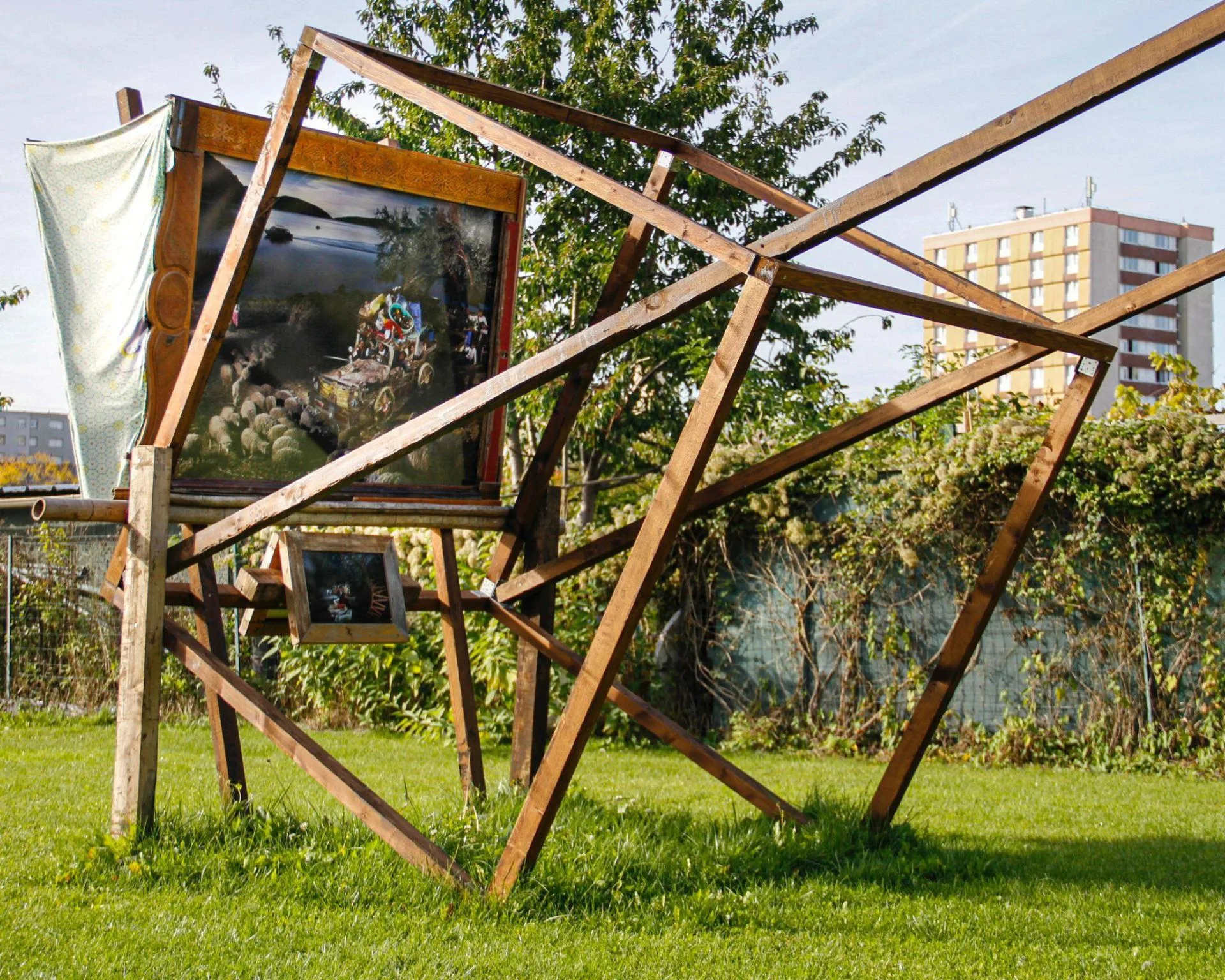 Une structure en bois aux poutres obliques porte deux tirages encadrés de Nicolas Henry, sur une pelouse au pied d'un immeuble, à Saint-Denis.