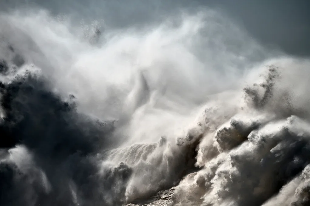 Une vague énorme se brise dans un nuage d'écume blanche et de bruine, sous un ciel gris, par Alessandro Puccinelli.