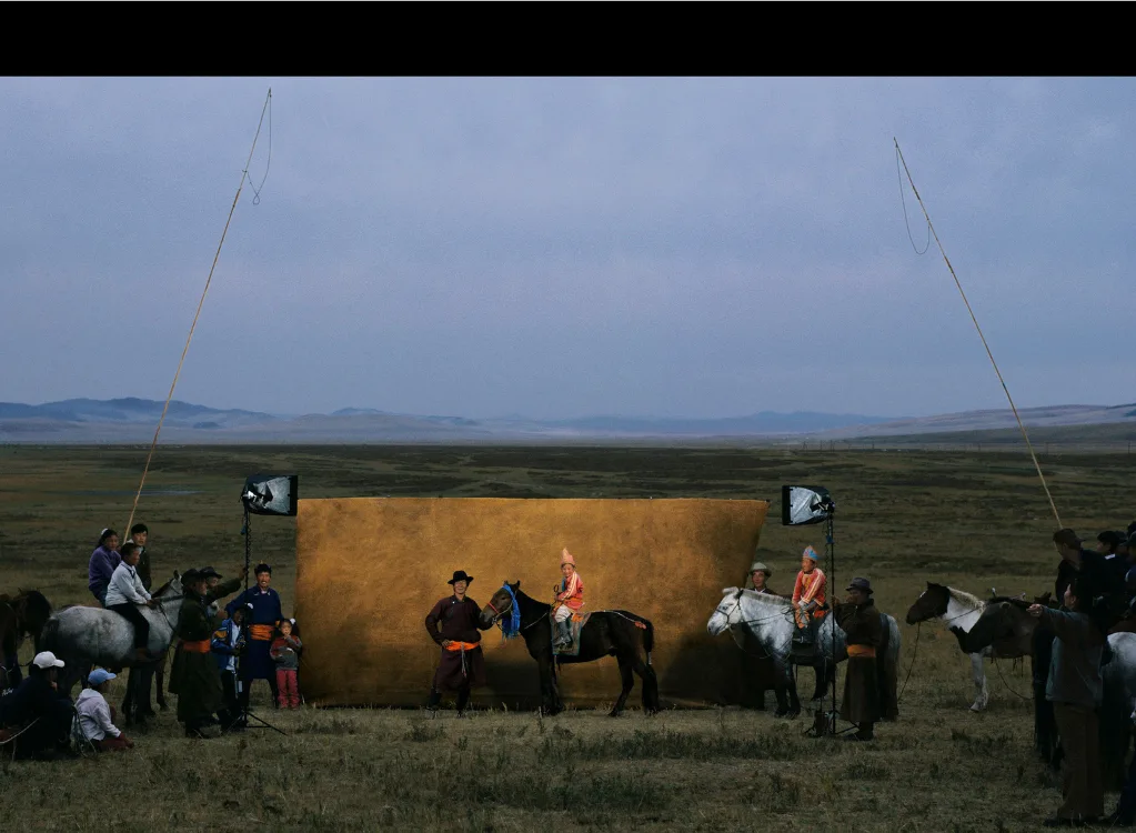 Coulisses d'une prise de vue de Yann Arthus-Bertrand dans la steppe : cavaliers et chevaux devant une grande toile dorée éclairée.