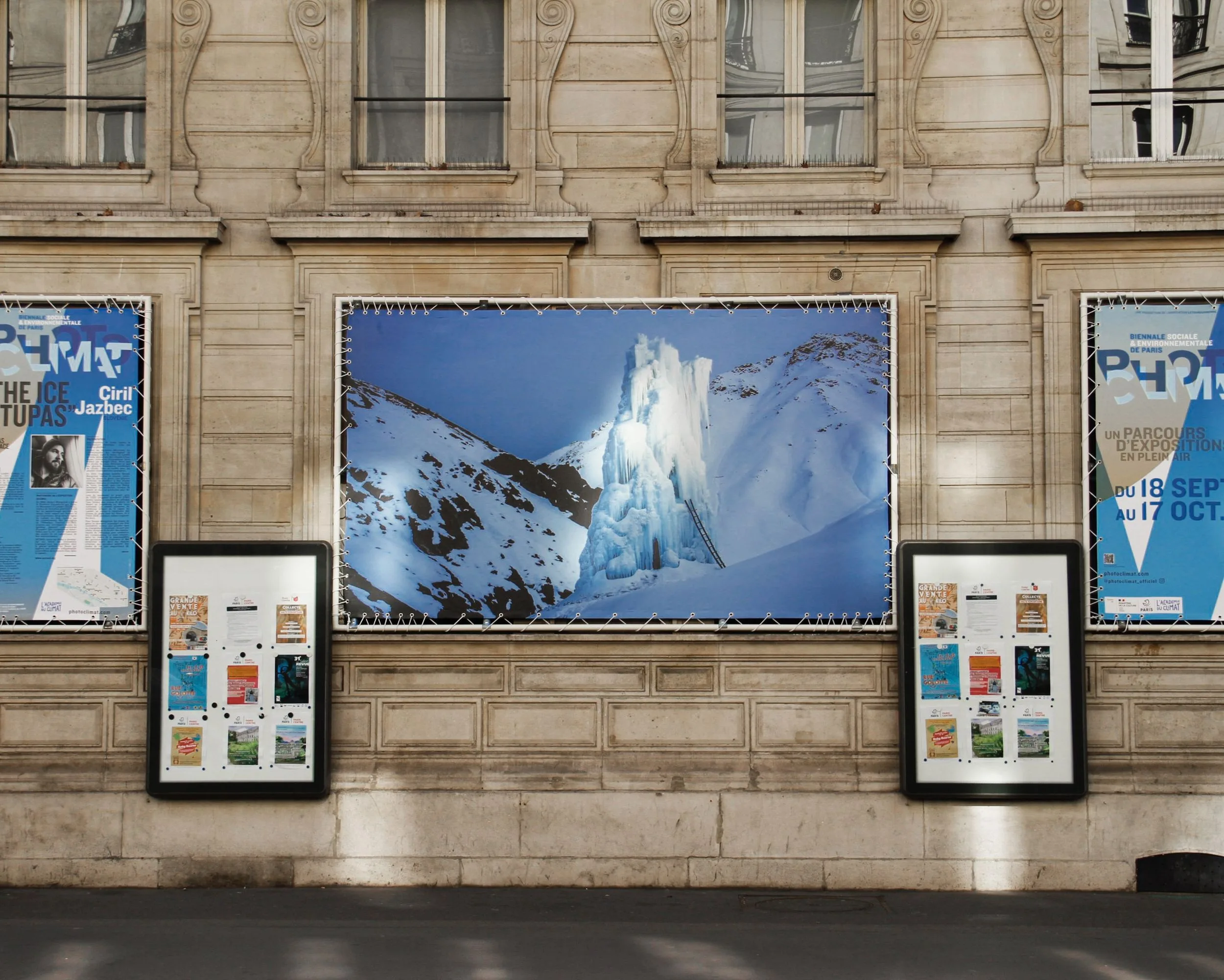 Grande bâche d'un stupa de glace de Ciril Jazbec sur la façade en pierre de l'Académie du Climat, entre deux affiches de Photoclimat.