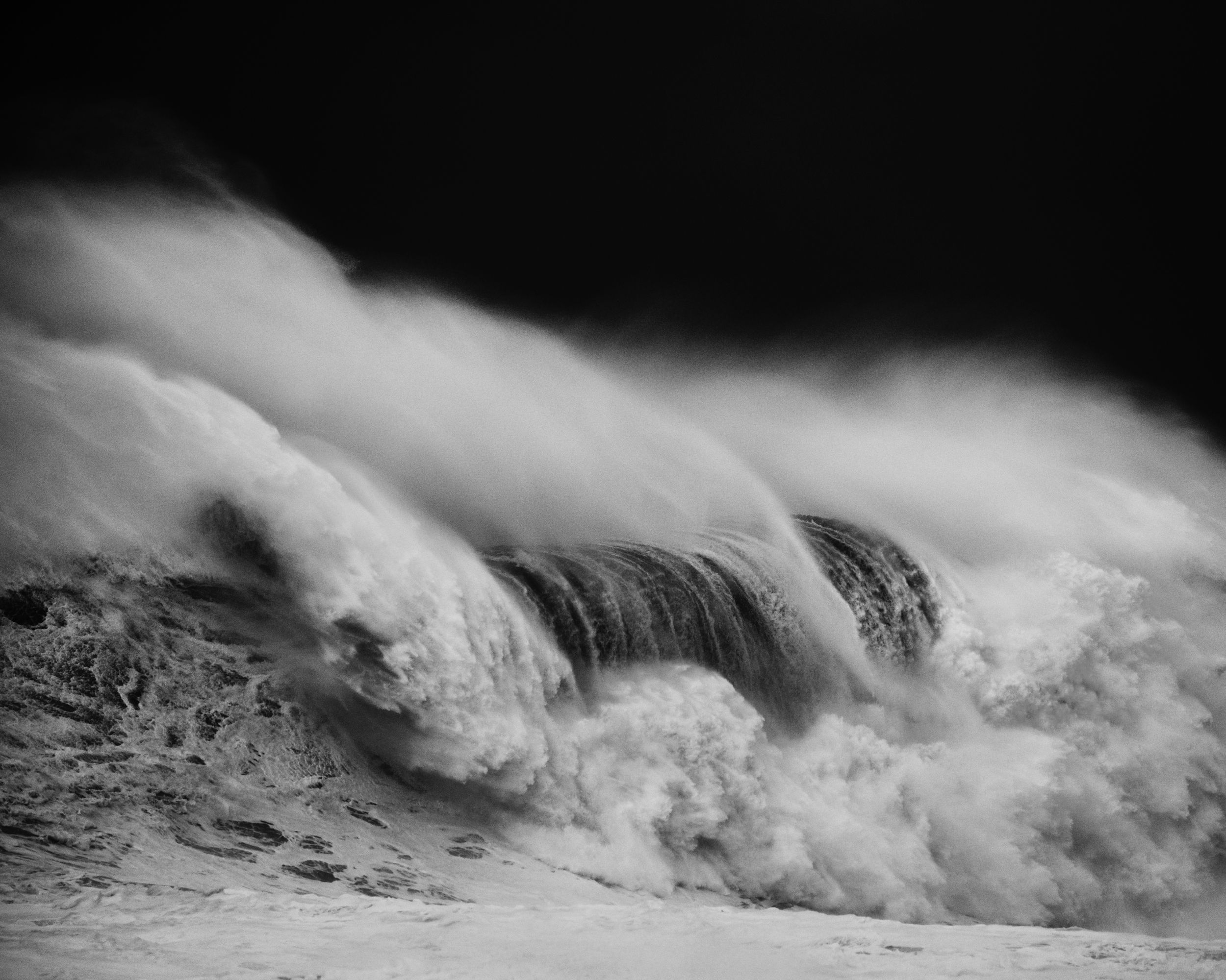 Vague de tempête en noir et blanc qui déferle, sa crête arrachée par le vent en longs voiles d'écume, par Alessandro Puccinelli.