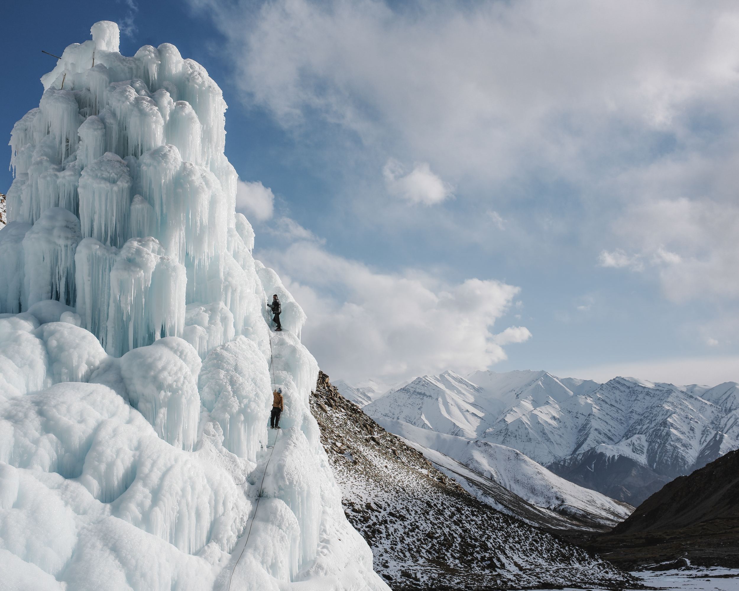 Deux personnes escaladent un immense stupa de glace, glacier artificiel du Ladakh, devant des montagnes enneigées, par Ciril Jazbec.