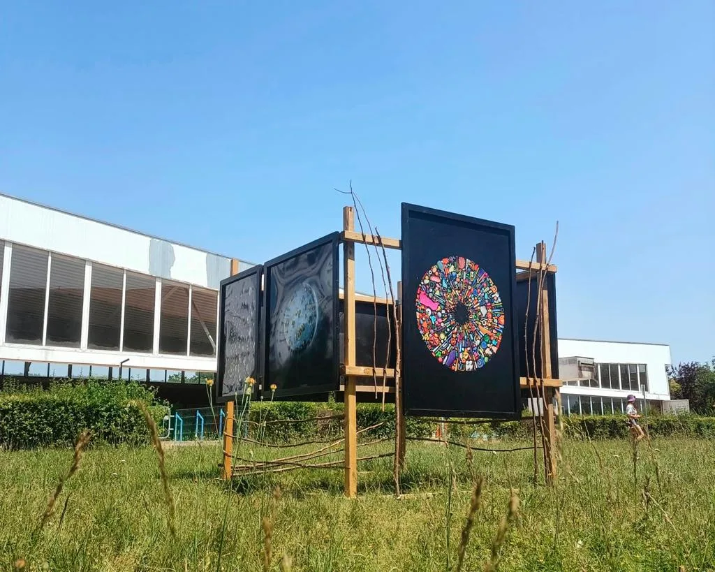 Trois tirages de Mandy Barker sur des cadres en bois plantés dans une prairie, devant le bâtiment vitré de la piscine de Bonneuil-sur-Marne.