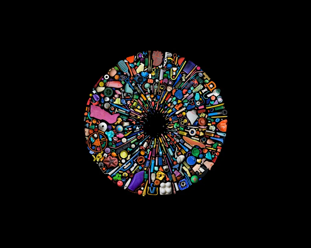 Disque de débris de plastique multicolores, bouchons, roues et jouets, disposés en rayons autour d'un centre noir, par Mandy Barker.