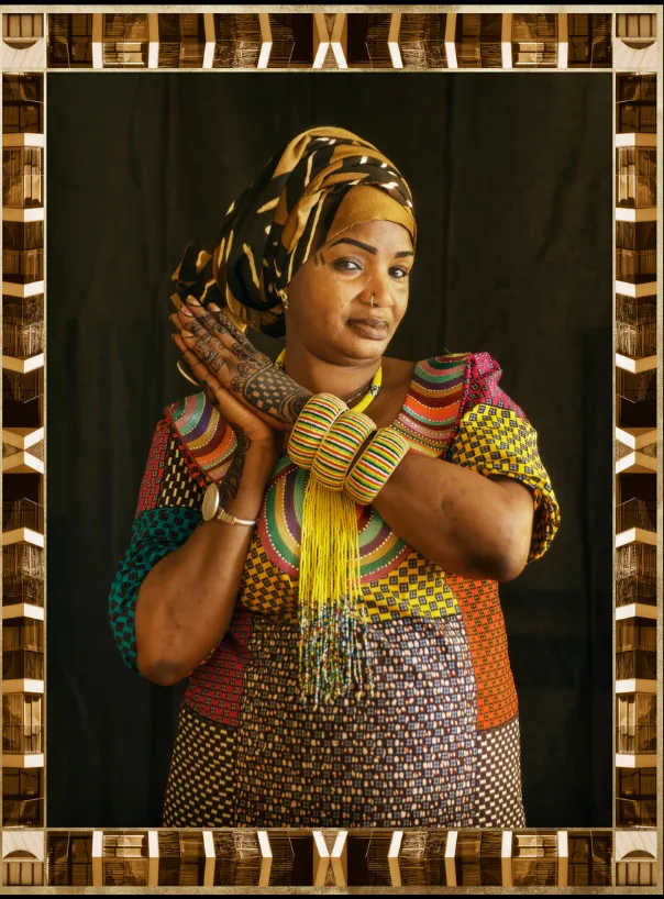 Portrait d'une femme au foulard noir et or, mains ornées de motifs croisées contre la joue, bracelets jaunes, dans un cadre doré.