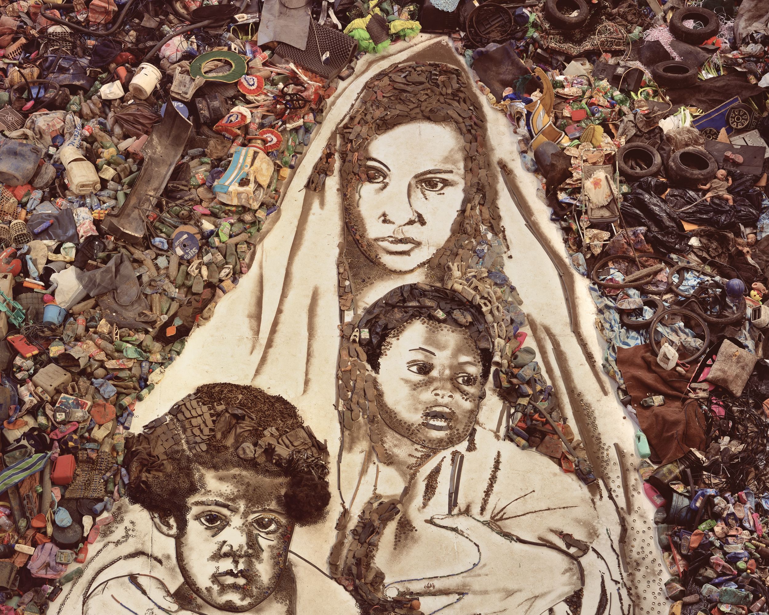 Portrait d'une mère et de deux enfants composé de déchets, posé au sol au milieu de plastiques, de pneus et d'objets jetés.
