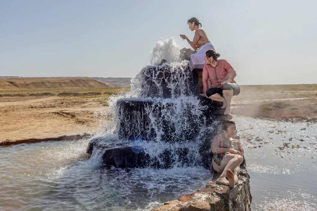 Trois femmes assises sur un rocher en gradins d'où jaillit une source d'eau, au milieu d'une steppe aride, par Anush Babajanyan.