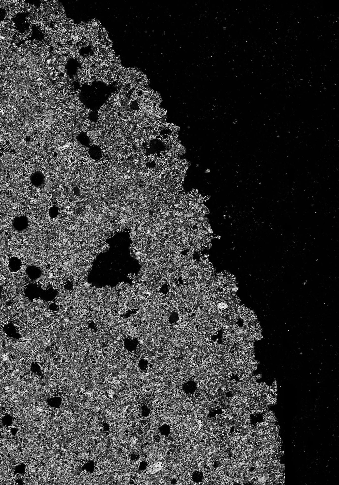 Texture minérale granuleuse en noir et blanc, criblée de trous, qui se détache sur un fond noir piqué de points blancs.