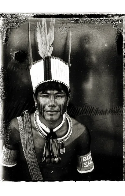Portrait noir et blanc d'un homme d'Amazonie coiffé d'une couronne de plumes blanches, le visage peint, colliers de perles au cou.