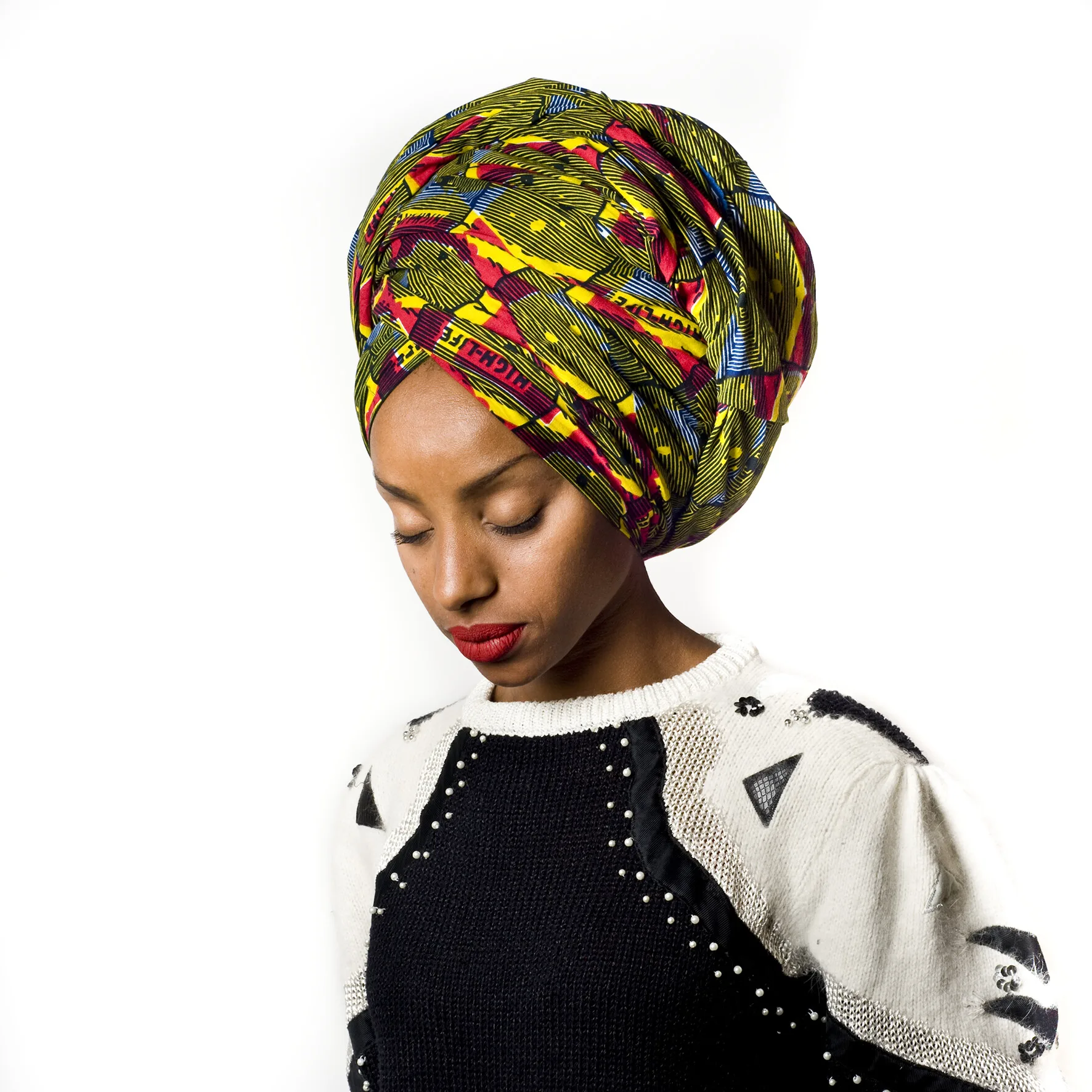 Portrait d'une jeune femme aux yeux baissés, coiffée d'un grand foulard imprimé jaune, vert et rouge, en pull noir et blanc perlé, par Hélène Jayet.