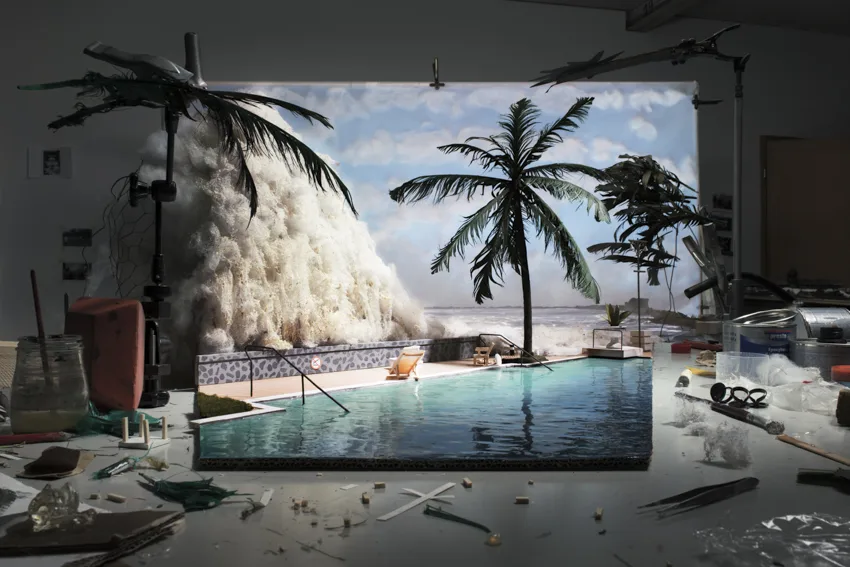 Maquette d'une piscine bordée de palmiers, frappée par une énorme vague d'écume, au milieu d'un atelier encombré, par Cortis et Sonderegger.