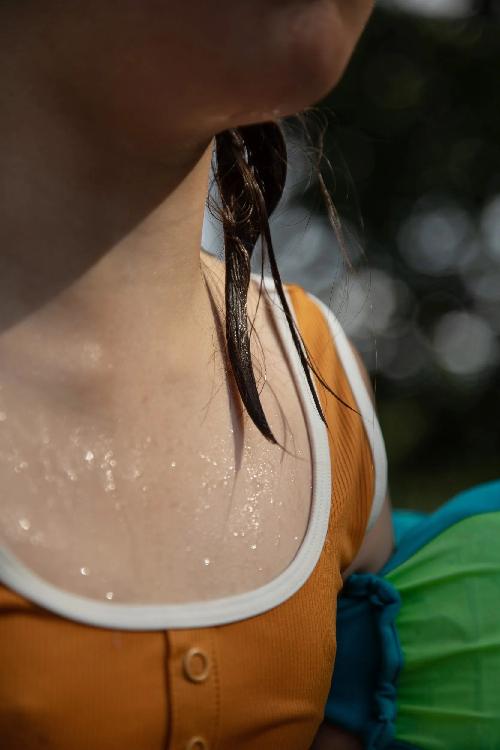 Gros plan sur le cou et l'épaule d'une personne perlés de gouttes d'eau, une mèche de cheveux mouillée sur un haut orange.