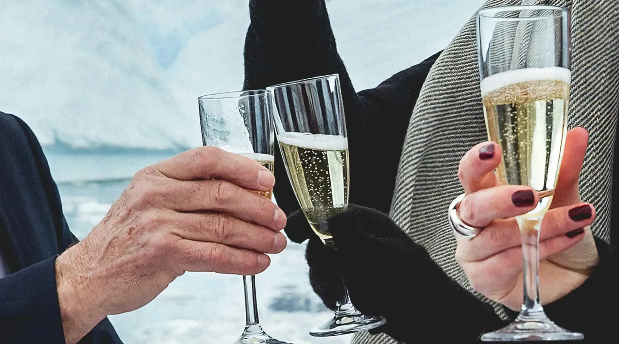 Des mains, l’une gantée, trinquent avec des flûtes de champagne devant un glacier.